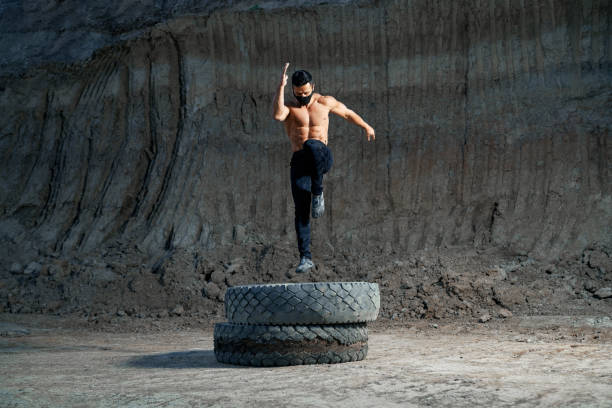 istock Handsome strong man jumping on wheel during evening workout 1292365748
