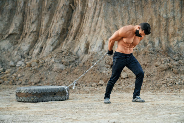 istock Strong man with naked chest pulling tyre on chain 1292365817