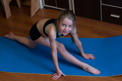 girl 8 years old with long hair in black sportwears  exercises around home  without equipment, sports activity at home