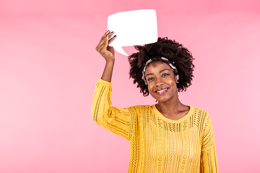 African American Woman showing sign speech bubble banner looking happy excited on pink background. Beautiful young joyful model on pink background having idea.