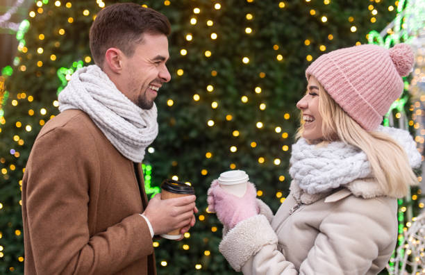 glückliches paar genießen heiße getränke in der nähe von weihnachtsbaum - communication discussion coffee christmas stock-fotos und bilder