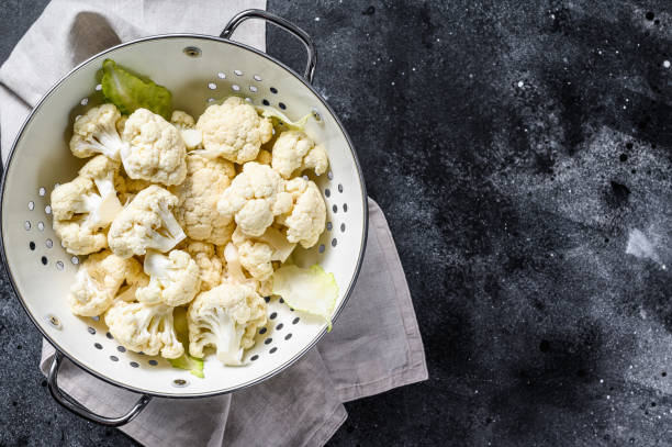 istock Washed fresh cauliflower cut into pieces in a colander. Black background. Top view. Copy space 1292369098