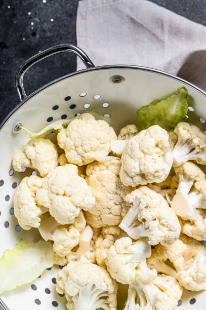 istock Washed fresh cauliflower cut into pieces in a colander. Black background. Top view 1292369113