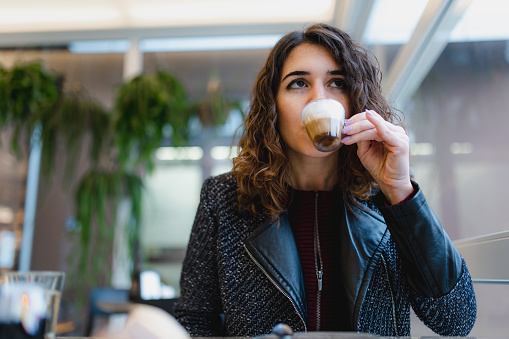 Close-up young caucasian woman in a cafe sitting in a table holding a cup of espresso coffee.