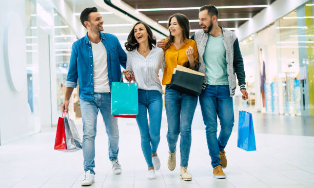 Happy group of excited beautiful modern stylish friends in casual wear with paper bags are walking in the mall during shopping. stock photo