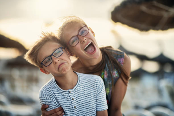 Happy kids embracing and smiling at the camera. Summer sunset on beach. The boy is making funny face.Nikon D850