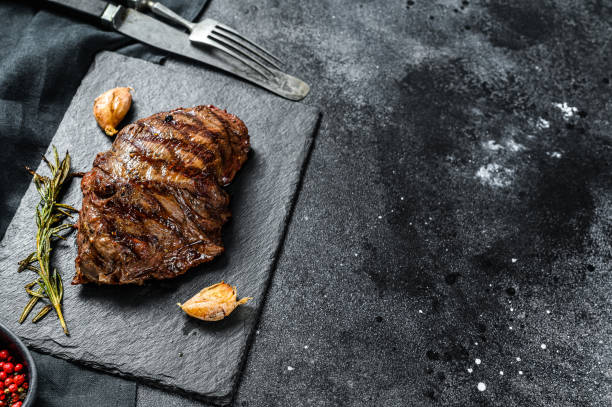 istock Grilled Flat Iron steak on a stone Board, marbled beef. Black background. Top view. Copy space 1292373140