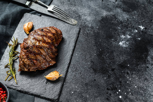 Grilled Flat Iron steak on a stone Board, marbled beef. Black background. Top view. Copy space Grilled Flat Iron steak on a stone Board, marbled beef. Black background. Top view. Copy space. barbecue beef stock pictures, royalty-free photos & images