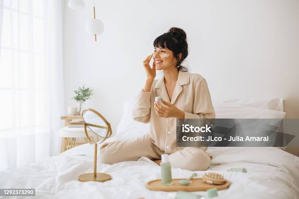 Smiling Woman Applying Face Cream Sitting On Bed Stock Photo - Download Image Now - Skin Care, One Woman Only, Beauty