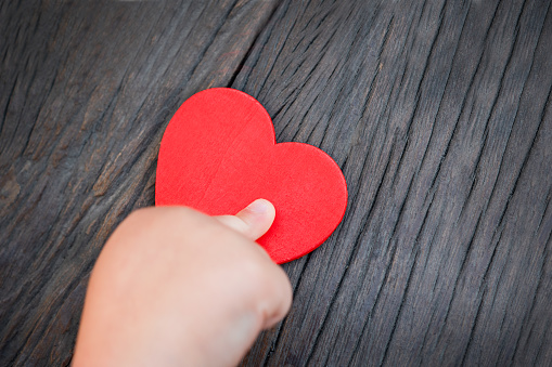 children's hand holding a red heart on a dark wooden background