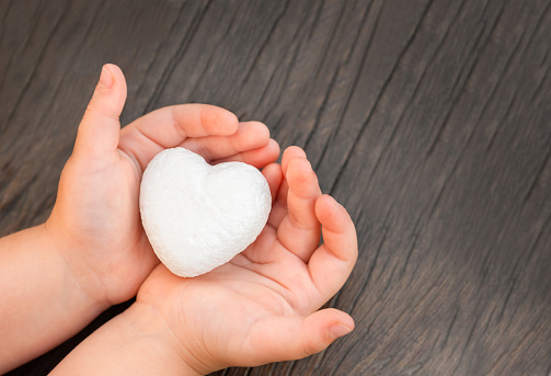 white foam heart in children's hands on a wooden background