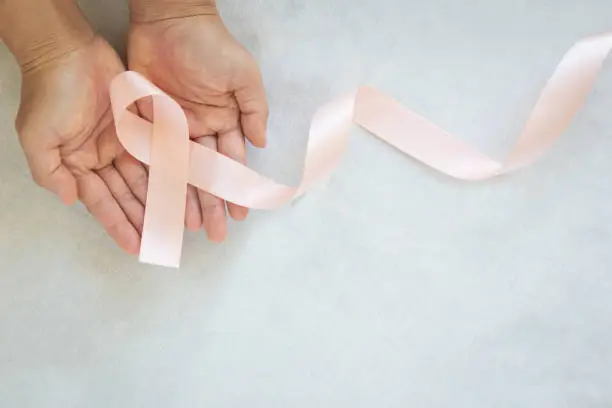 Hand holding Peach color ribbon curl on white fabric background with copy space, symbol for Uterine and Endometrial cancer awareness, World Cancer Day. Healthcare or hospital and insurance concept.