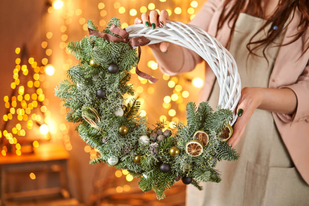 jeune femme retenant une boucle de couronne de noël a décoré des branches de sapin et des jouets de noël pour la fête. la célébration du nouvel an. magasin de fleurs européen - couronne de noel artisanale photos et images de collection