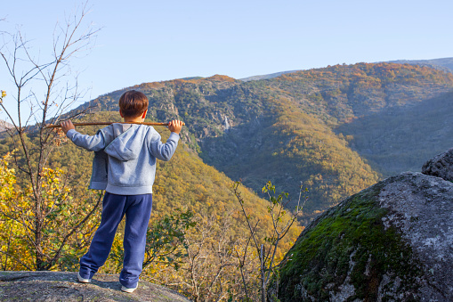 Child boy observing the Chorrero de la Virgen waterfall at Natural Reserve Garganta de los Infiernos, Extremadura, Spain. He holds a cane over his shoulders