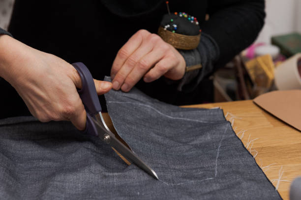 istock Human hands cutting out the template of fabric with dressmaker shear for making protective face masks at home during lockdown of Covid crisis 1292375450