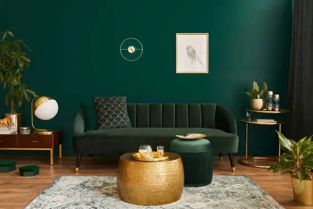Photo of Luxury living room in house with modern interior design, green velvet sofa, coffee table, pouf, gold decoration, plant, lamp, carpet, mock up poster frame and elegant accessories. Template.