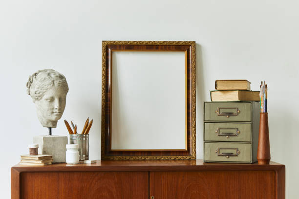 istock Stylish composition of artist workspace room with design retro teak commode, mock up poster frame, book, decoration and painting accessories. Template. 1292378148
