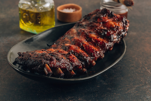 Homemade barbecued ribs seasoned with a spicy basting sauce and served on a black plate over dark background. Selective focus