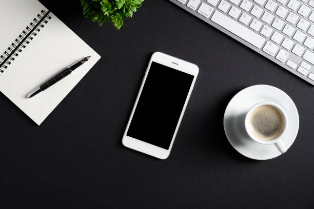istock Black office desk table top view. Flat lay smartphone with blank screen mockup, computer keyboard, cup of coffee, paper notepad. Blogger workspace. Business concept. 1292382248