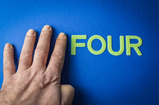 Four human fingers beside the word Four written with plastic letters on blue paper background, concept