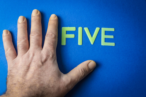Five human fingers beside the word Five written with plastic letters on blue paper background, concept