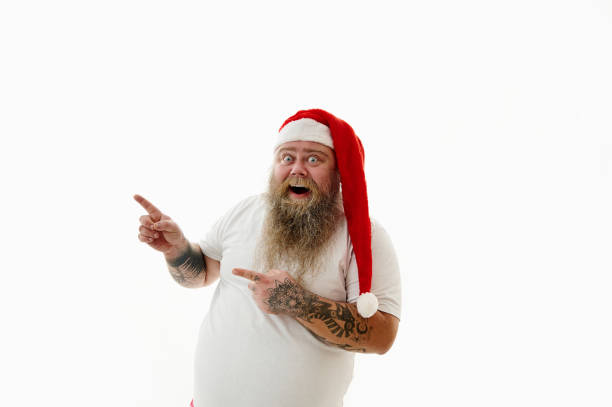 Isolated portrait on a white background of an overweigh man in Santa Claus hat gesturing with finger. copy space Portrait on a white background of an overweigh man in Santa Claus hat gesturing with finger. Copy Space arm tattoo ideas for men pictures stock pictures, royalty-free photos & images