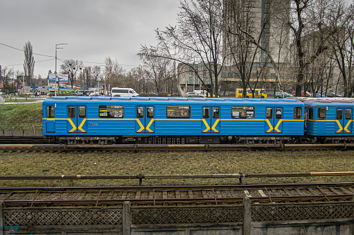 Kyiv, Ukraine - December, 2020: Side view of a blue subway train with yellow stripes, outdoors on a cloudy autumn day.