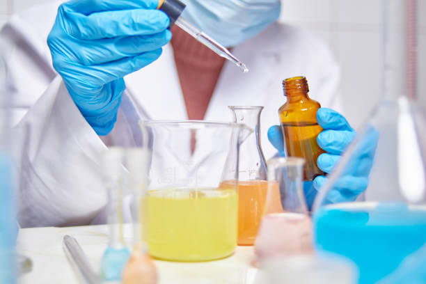 istock lab technician in white coat, blue gloves and face mask doing experiments and tests in a laboratory with different colored substances 1292383711