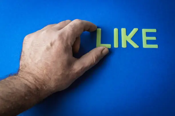 Photo of Human fingers picking the word Like written with plastic letters on blue paper background, concept