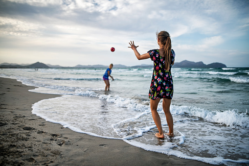 Mother and daughter playing with the ball on the beach.\nNikon D850
