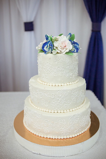 Three-tier white wedding cake decorated with white and blue flowers. Beautiful and stylish wedding cake. A cake with a beautiful decor.