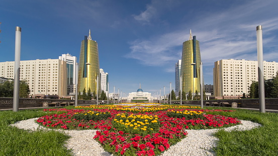 A square in front of Ak Orda with Altyn Orda business center timelapse hyperlapse in the foreground with flowerbed. Ak Orda is the presidential residence in Astana, the capital of Kazakhstan. 4K
