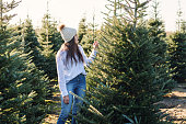 Beautiful smiling girl chooses a Christmas tree on garden centre outdoors before winter holidays.
