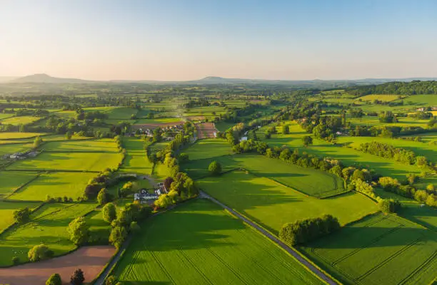 Warm sunset light illuminating the picturesque patchwork quilt landscape of green pasture, agricultural crops, farms and villages below clear blue panoramic skies.