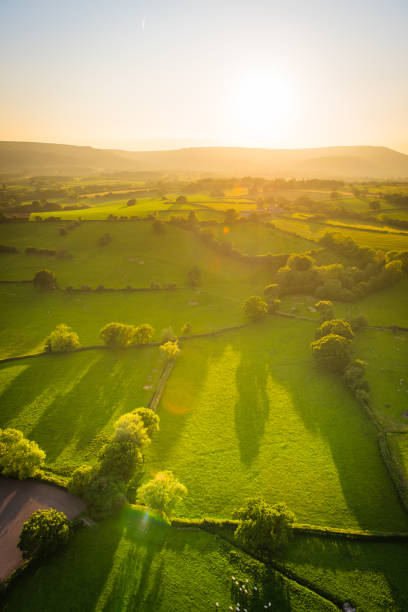 Aerial photograph over green farm pasture golden sunlight on mountain Warm light of sunset illuminating the picturesque patchwork quilt landscape of green pasture, agricultural crops, farms, villages and the distant mountains of South Wales, UK. patchwork landscape stock pictures, royalty-free photos & images