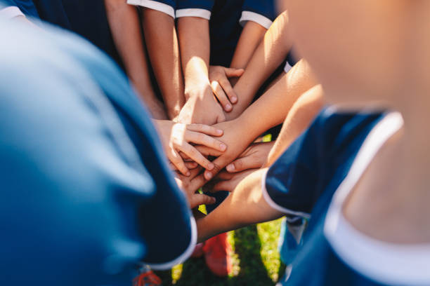 groupe d’enfants heureux dans l’équipe sportive empilant des mains en plein air dans une journée d’été. sports d’équipe pour enfants. garçons au camp sportif empilant des mains avant un jeu. enfants d’âge scolaire dans une équipe au domai - capitaine déquipe photos et images de collection