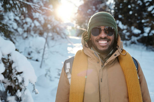 寒さを楽しむサングラスと暖かいウィンターウェアで幸せな若いアフリカ人男性 - snow glasses ストックフォトと画像