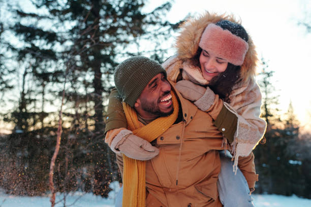 ragazzo africano ridendo in abbigliamento invernale dando alla sua ragazza piggyback all'aperto - fun knit hat adult dating foto e immagini stock