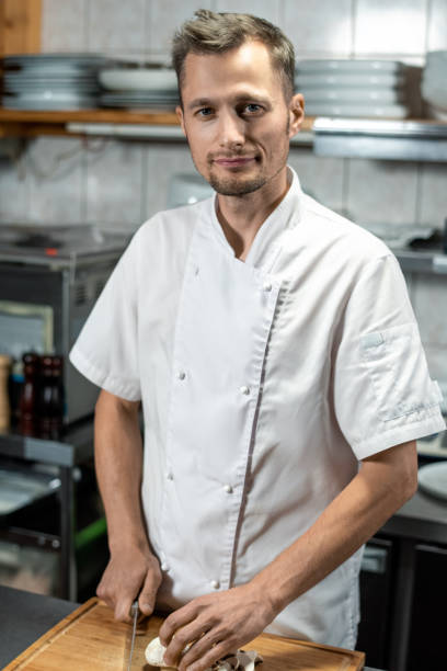istock Young professional male chef in white uniform looking at you while cooking 1292402417