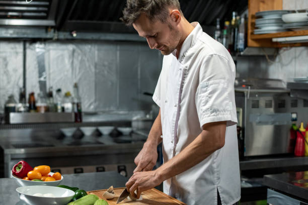 istock Young professional chef of modern restaurant in uniform cutting vegetables 1292402425