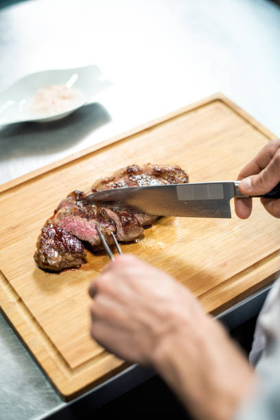 istock Hands of chef with sharp knife cutting roasted beef steak on wooden board 1292402428