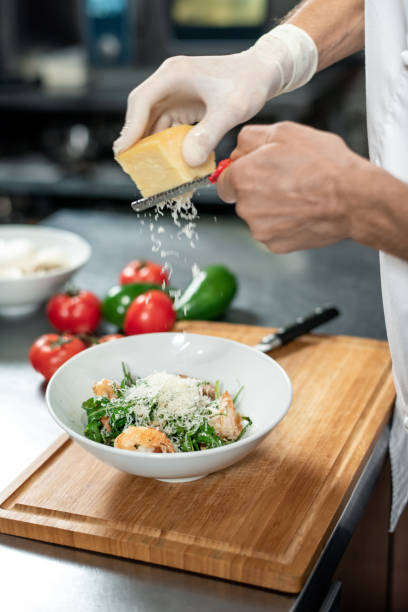 istock Hands of chef in uniform grating fresh cheese into ceramic bowl containing salad 1292402439