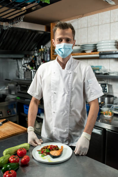 istock Young professional chef in white uniform and protective mask ready to serve food 1292402470