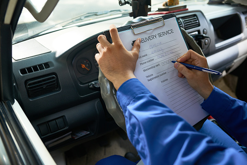 Hands of courier filling delivery service document when sitting in truck