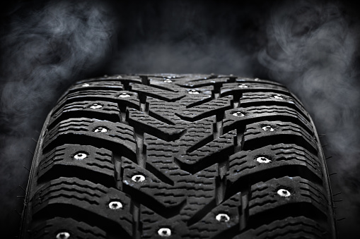 winter studded tyre dark moody. steam on background. studio shot. tyres industry concept. copy space