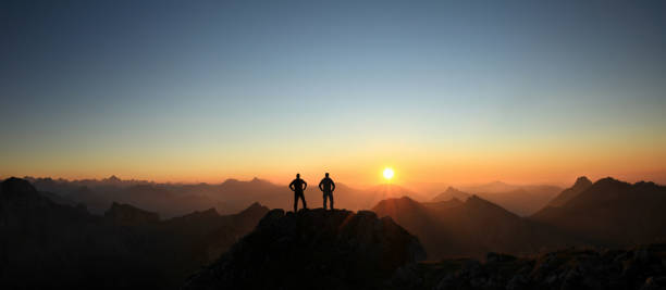 Two Men reaching summit enjoying freedom and looking towards mountains sunset. Happy winning success men at sunset or sunrise standing relaxed and are happy for having reached mountain top summit goal during hiking travel trek. Tirol, Austria. Allgau, Bavaria. bavarian alps photos stock pictures, royalty-free photos & images