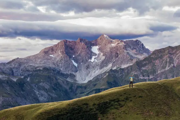 Young Man hikes at majestic Karkopf mountain in the first daylight. Purple light illuminates landscape and the moody sky. Karkopf, Lechtal Alps, Vorarlberg, Allgau, Austria.