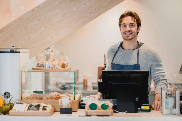 istock Smiling attractive young waiter standing at cafe counter in small cafeteria 1292406072