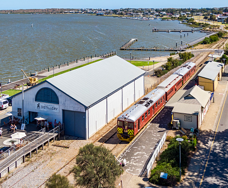 Goolwa, Australia - Dec 20, 2020: Aerial view Cockle Train with SteamRanger Heritage Railway vintage Redhen railcars departing the historic Goolwa Port Railway Station with the Fleurieu Distillery in the old Goods Shed. The train has Christmas tinsel decorations