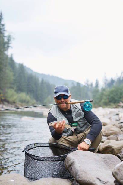 istock Fisherman holding trout while sitting on stones near river 1292406080